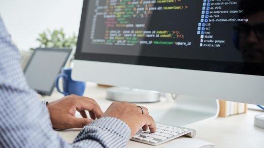 Programista pisze kod na komputerze z dwoma monitorami w biurze.