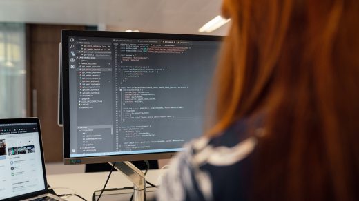 Osoba analizująca kod źródłowy na monitorze komputera w biurze